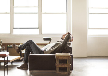 Seitenansicht eines Geschäftsmannes, der sich auf einem Sofa in einem hell erleuchteten, kreativen Büro entspannt - CAVF43268