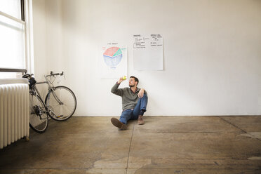 Businessman holding ball while sitting against charts on wall in creative office - CAVF43280