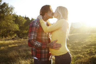 Romantisches Paar, das sich küsst, während es auf einer Wiese in der Sonne steht - CAVF43315