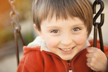 Portrait of cheerful boy playing on swing at park - CAVF43321