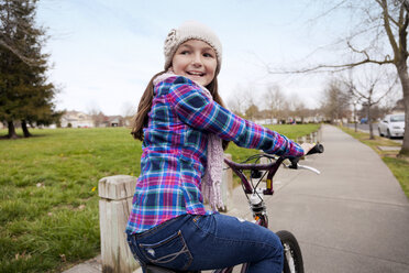 Glückliches Mädchen Radfahren auf der Straße durch grasbewachsenen Feld gegen Himmel - CAVF43357
