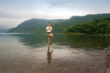 Full length of woman doing yoga on rock amidst lake by mountains - CAVF43363