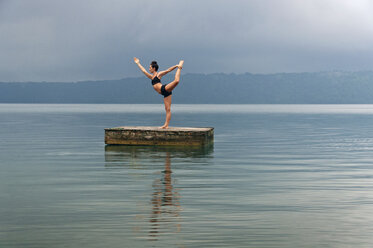 Frau in Königstänzerin Pose tun Yoga auf schwimmenden Plattform inmitten See gegen Himmel - CAVF43364
