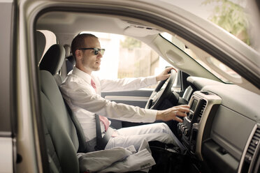 Side view of gay man wearing suit riding car on sunny day - CAVF43367