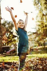 Fröhliches Mädchen spielt mit Blättern im Park im Herbst - CAVF43413