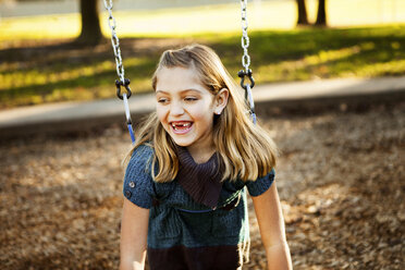 Cheerful girl playing on swing at park during autumn - CAVF43416