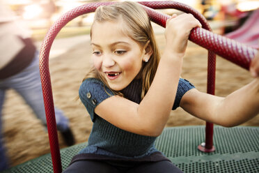 Happy girl playing on merry-go-round at park - CAVF43417