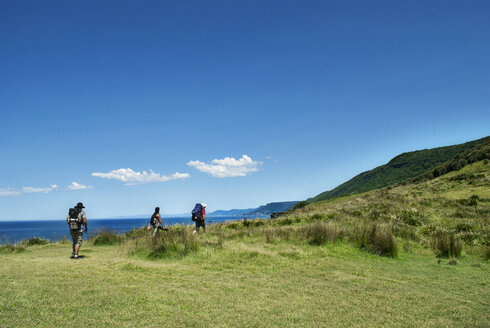 Hikers climbing mountain by sea against blue sky - CAVF43433