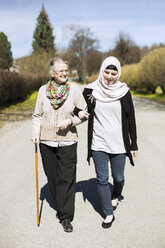 Ältere Frau in voller Länge mit weiblicher Betreuerin zu Fuß Arm in Arm auf der Straße - MASF05605