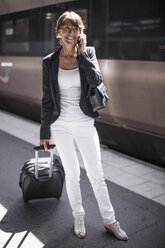 Glückliche Geschäftsfrau mit Koffer und Mobiltelefon auf dem Bahnsteig - MASF05610