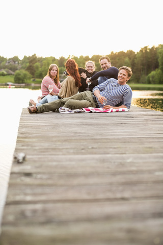 Eine Gruppe von Freunden entspannt sich auf einem Pier am See, lizenzfreies Stockfoto