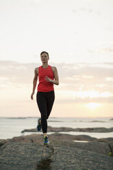 Full length of woman running on rocks at seaside - MASF05627