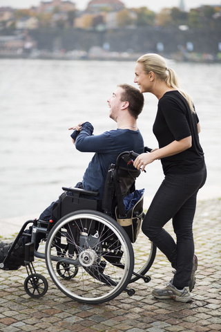 Happy disabled man with caretaker enjoying view by lake stock photo
