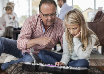 Großvater und Enkelin spielen Klavier mit der Familie im Hintergrund zu Hause - MASF05640