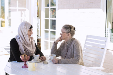 Female home caregiver and senior woman conversing while having coffee on porch - MASF05663