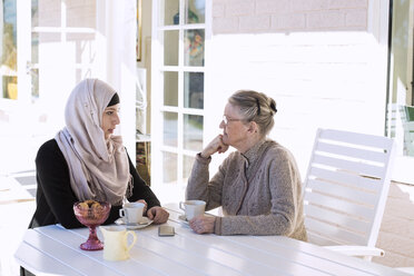 Hauspflegerin und ältere Frau unterhalten sich beim Kaffee auf der Veranda - MASF05663