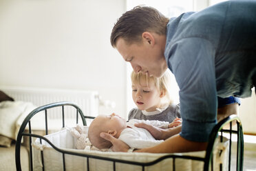 Father putting baby girl in cradle while daughter looking at them - MASF05669