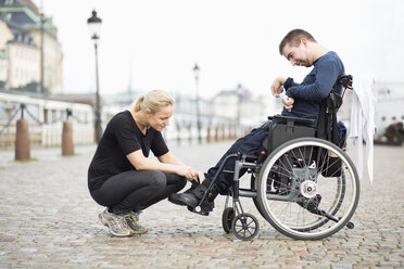 Female caretaker putting on disabled man's shoes on street - MASF05677