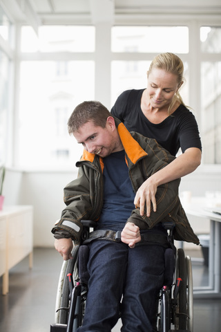 Hausmeisterin hilft einem behinderten Mann im Rollstuhl zu Hause, lizenzfreies Stockfoto