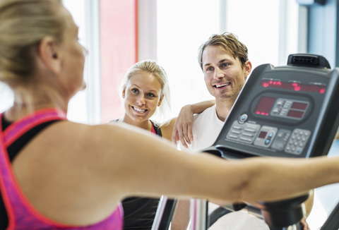 Freunde schauen auf eine Frau, die im Fitnessstudio auf dem Laufband trainiert, lizenzfreies Stockfoto