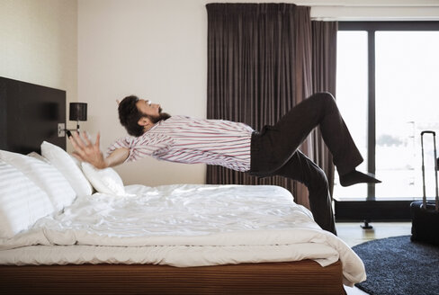 Geschäftsmann springt in voller Länge auf das Bett im Hotelzimmer - MASF05690