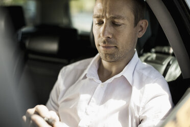 Geschäftsmann, der im Taxi eine Textnachricht über sein Mobiltelefon verschickt - MASF05708