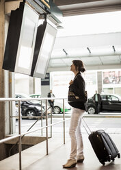 Businesswoman looking at arrival departure board on railway station - MASF05714