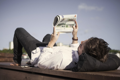 Geschäftsmann liest Zeitung, während er auf der Strandpromenade liegt, lizenzfreies Stockfoto