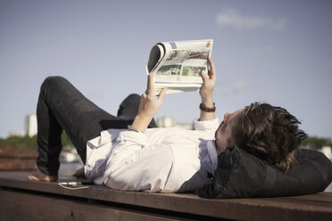 Businessman reading newspaper while lying on boardwalk - MASF05716