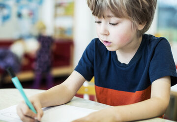 Junge zeichnet auf Papier am Tisch im Kindergarten - MASF05804