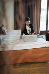 Geschäftsfrau mit Laptop auf dem Bett im Hotelzimmer - MASF05810