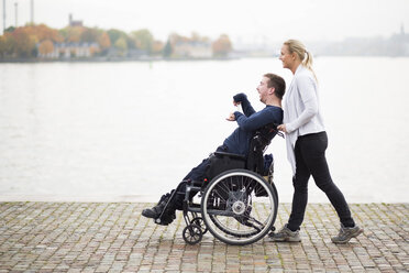 Caretaker pushing disabled man on wheelchair along lake - MASF05860