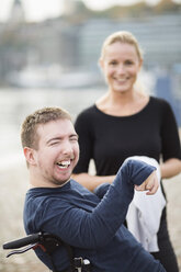 Disabled man on wheelchair laughing by caretaker outdoors - MASF05862