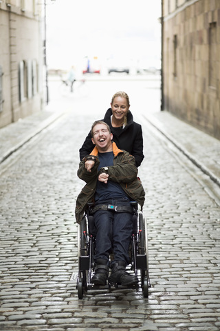 Hausmeister schiebt behinderten Mann im Rollstuhl durch die Stadt, lizenzfreies Stockfoto