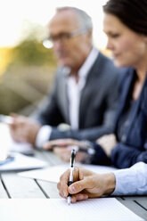 Cropped image of businessman writing on document with colleagues at table - MASF05875