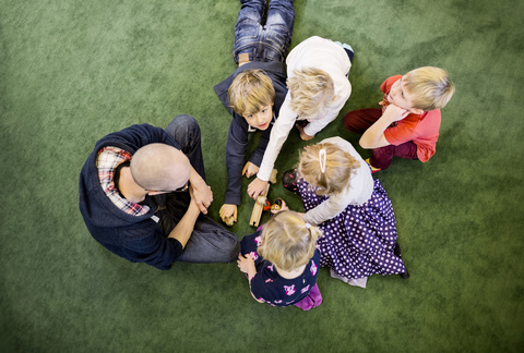 Direkt über der Aufnahme einer Lehrerin mit Schülern, die auf einem Teppich im Kindergarten spielen, lizenzfreies Stockfoto