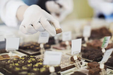 Ausgeschnittenes Bild eines Arbeiters, der Süßigkeiten in einer Vitrine in einem Café hält - MASF05888