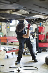 Young mechanic repairing car from below at auto repair shop - MASF05900