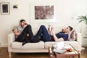 Junger schwuler Mann liest ein Buch, während sein Partner ihn auf dem Sofa ansieht - MASF05937