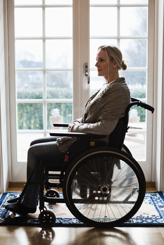 Seitenansicht einer behinderten Frau im Rollstuhl zu Hause, lizenzfreies Stockfoto