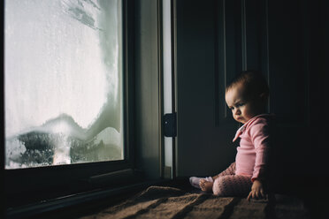 Kleines Mädchen, das zu Hause an einer Glastür mit Beschlag sitzt - CAVF43470