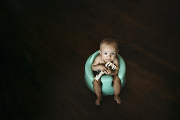 High angle portrait of baby girl with toy sitting on potty at home - CAVF43476