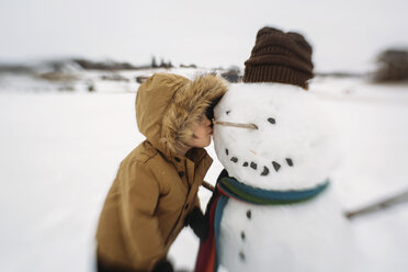 Junge küsst Schneemann, während er auf einem Feld vor dem Himmel steht - CAVF43483