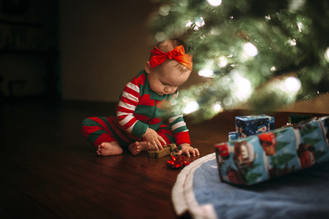 Mädchen spielt mit Spielzeug, während sie zu Hause am Weihnachtsbaum sitzt, lizenzfreies Stockfoto