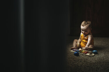Baby girl playing xylophone while sitting on rug at home - CAVF43495