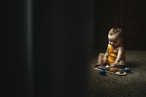 Baby-Mädchen spielt Xylophon und sitzt auf einem Teppich zu Hause - CAVF43495
