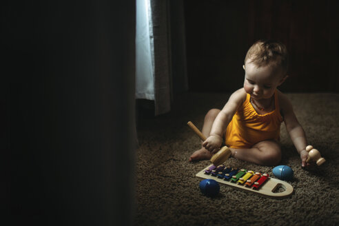 Baby girl playing xylophone on rug at home - CAVF43496