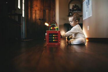 Baby-Mädchen spielt mit Abakus, während sie auf dem Boden zu Hause sitzt - CAVF43499