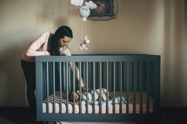 Mother looking at daughter sleeping in crib at home - CAVF43500