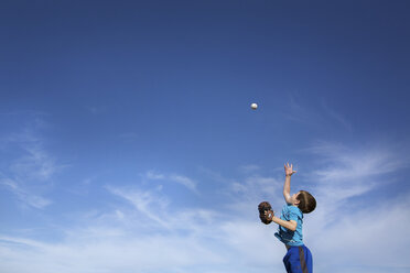 Low angle view of boy playing baseball against blue sky during sunny day - CAVF43504